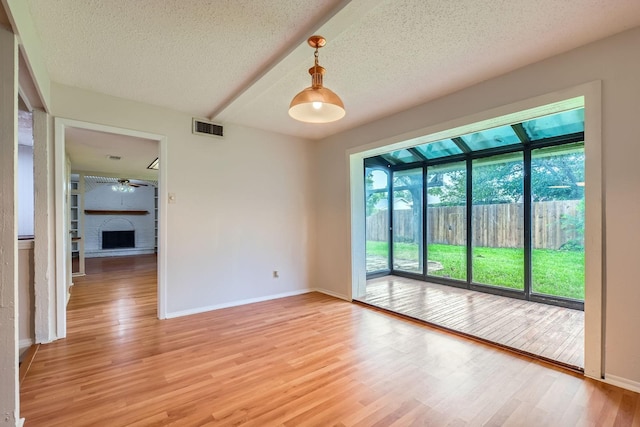902 Via Valencia, Mesquite, TX 75150 - unfurnished room featuring light wood-type flooring, a brick fireplace, a textured ceiling, and ceiling fan