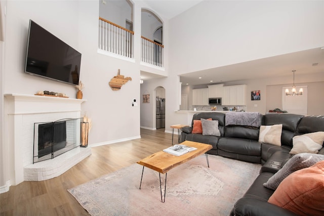 12720 Outlook Ave, Fort Worth, TX 76244 - living room with a chandelier, light wood-style flooring, a brick fireplace, arched walkways, and a high ceiling