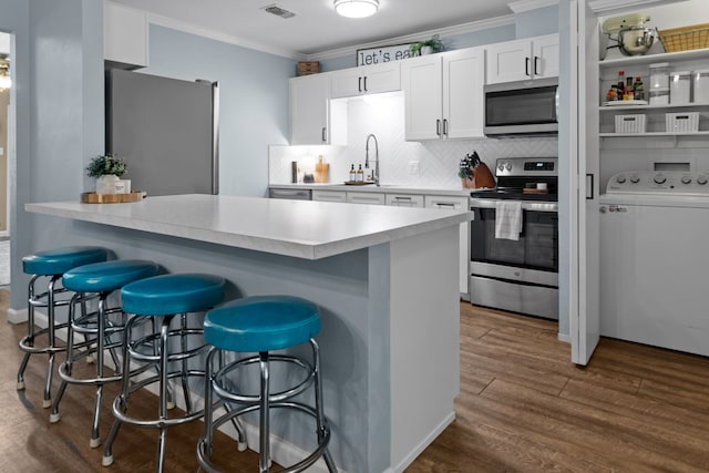 5807 Shady Hill Ln, Arlington, TX 76016 - kitchen featuring stainless steel appliances, washer / clothes dryer, ornamental molding, a kitchen breakfast bar, and white cabinets