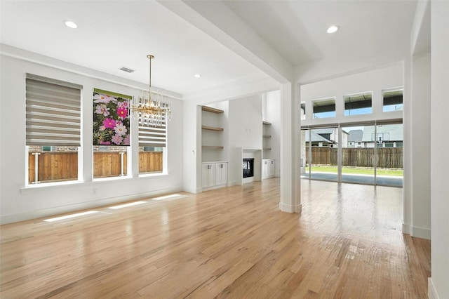 13868 Dorset Ln, Frisco, TX 75035 - unfurnished living room featuring built in shelves, a chandelier, light wood finished floors, recessed lighting, and a glass covered fireplace