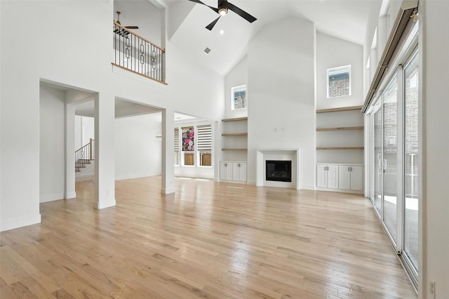 13868 Dorset Ln, Frisco, TX 75035 - unfurnished living room with a ceiling fan, stairway, light wood-type flooring, high vaulted ceiling, and a glass covered fireplace