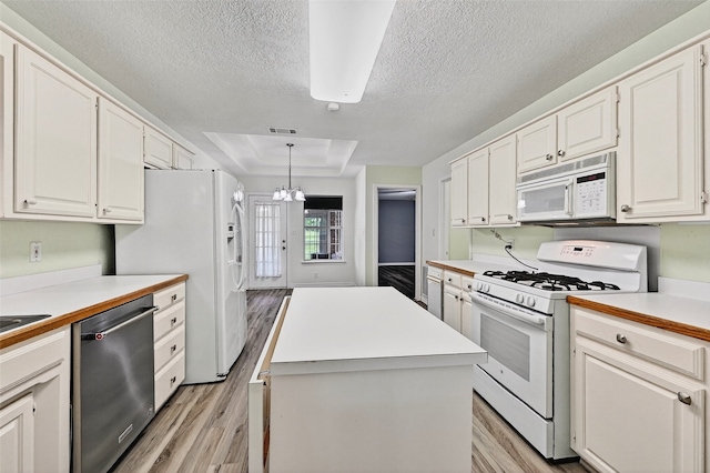 2107 Meadows Cir, Sherman, TX 75092 - kitchen with white appliances, light wood-style flooring, a textured ceiling, a tray ceiling, and a center island