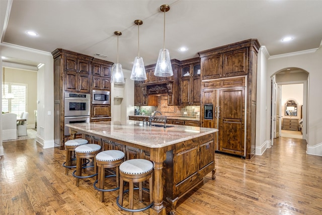 2521 Fair Oaks Ln, Prosper, TX 75078 - kitchen featuring built in appliances, arched walkways, light wood-style floors, tasteful backsplash, and light stone countertops