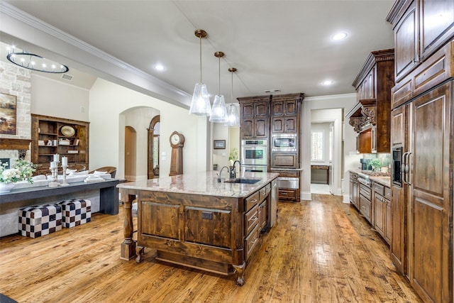 2521 Fair Oaks Ln, Prosper, TX 75078 - kitchen with arched walkways, built in appliances, ornamental molding, light wood-type flooring, and a center island with sink