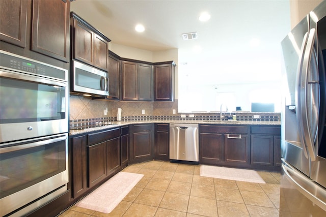 9929 Caney Creek Dr, Waco, TX 76708 - kitchen with stainless steel appliances, dark brown cabinets, tasteful backsplash, light stone counters, and light tile patterned flooring