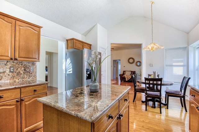 3104 Park Garden Pl, Richardson, TX 75082 - kitchen with stainless steel fridge, light stone counters, brown cabinetry, a kitchen island, and high vaulted ceiling