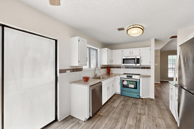 10320 Wood Heights Dr, Dallas, TX 75227 - kitchen featuring appliances with stainless steel finishes, white cabinets, light wood finished floors, light countertops, and decorative backsplash