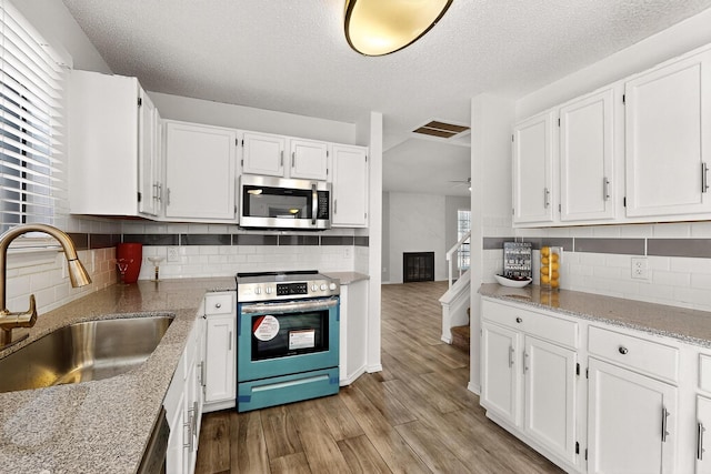 10320 Wood Heights Dr, Dallas, TX 75227 - kitchen with appliances with stainless steel finishes, white cabinetry, decorative backsplash, and a textured ceiling