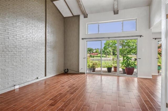 1822 Lakecrest Ct, Carrollton, TX 75006 - empty room featuring a high ceiling, beamed ceiling, healthy amount of natural light, wood finished floors, and brick wall