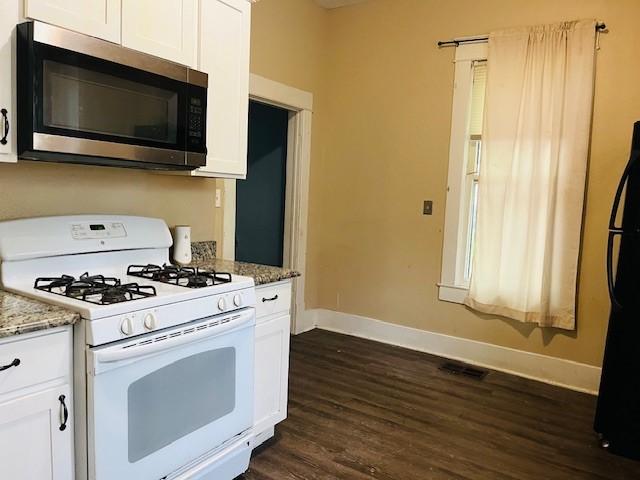 106 Lawrence Ave, Terrell, TX 75160 - kitchen with stainless steel microwave, white gas stove, freestanding refrigerator, dark wood-style floors, and white cabinets
