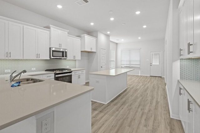 2105 Hazel Lily Run, Mesquite, TX 75181 - kitchen with appliances with stainless steel finishes, white cabinetry, a kitchen island, tasteful backsplash, and light wood finished floors