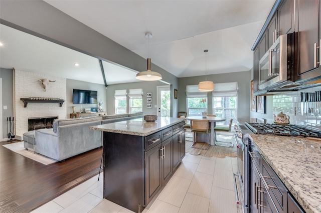 9126 Valley Chapel Ln, Dallas, TX 75220 - kitchen featuring appliances with stainless steel finishes, light stone counters, hanging light fixtures, a fireplace, and a center island