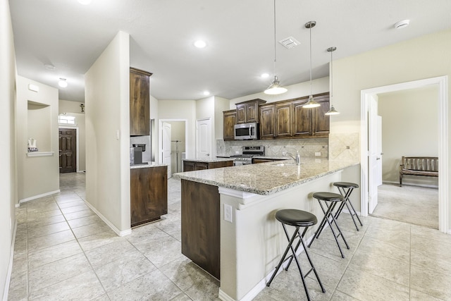 2600 Canyon Wren Ln, Fort Worth, TX 76244 - kitchen with stainless steel appliances, a kitchen bar, light tile patterned floors, decorative backsplash, and dark brown cabinets