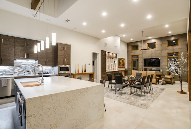 548 Oak Grove Ln, Coppell, TX 75019 - kitchen featuring stainless steel appliances, decorative light fixtures, a center island with sink, decorative backsplash, and dark brown cabinets