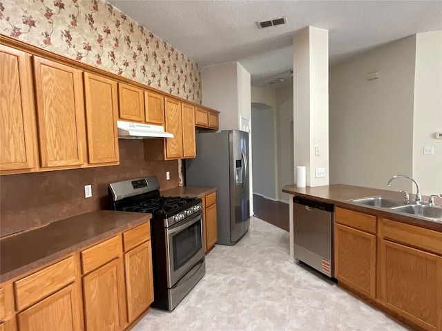 939 Clear Creek Dr, Mesquite, TX 75181 - kitchen with appliances with stainless steel finishes, under cabinet range hood, light floors, wallpapered walls, and dark countertops