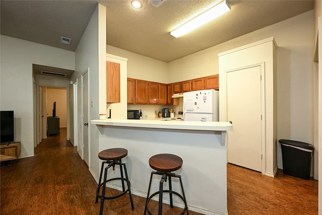 1113-1115 Bayfield Dr, Denton, TX 76209 - kitchen featuring freestanding refrigerator, dark wood-style floors, brown cabinets, a kitchen bar, and a textured ceiling
