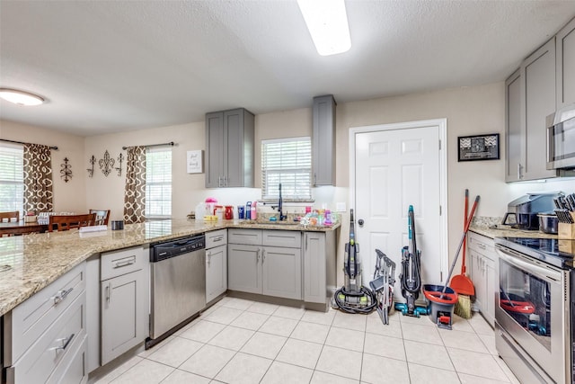 318 E Chestnut St, Denison, TX 75021 - kitchen with stainless steel appliances, gray cabinets, a peninsula, light stone counters, and a textured ceiling