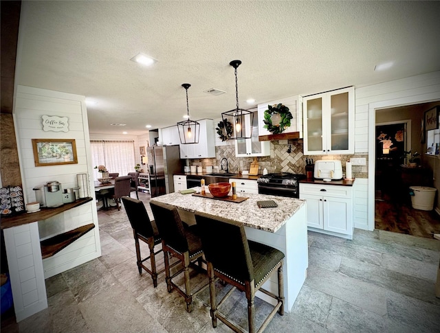 4124 Maryview Ct, Haltom City, TX 76117 - kitchen featuring black range with gas stovetop, stainless steel fridge, a kitchen island, a breakfast bar, and white cabinetry