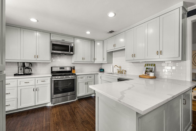 4903 Wateka Dr, Dallas, TX 75209 - kitchen featuring stainless steel appliances, a peninsula, dark wood-style floors, decorative backsplash, and recessed lighting