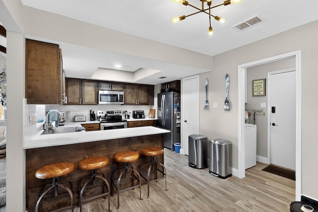 5700 Kingstree Ct, Arlington, TX 76017 - kitchen featuring appliances with stainless steel finishes, dark brown cabinets, light wood-style flooring, a breakfast bar area, and light countertops