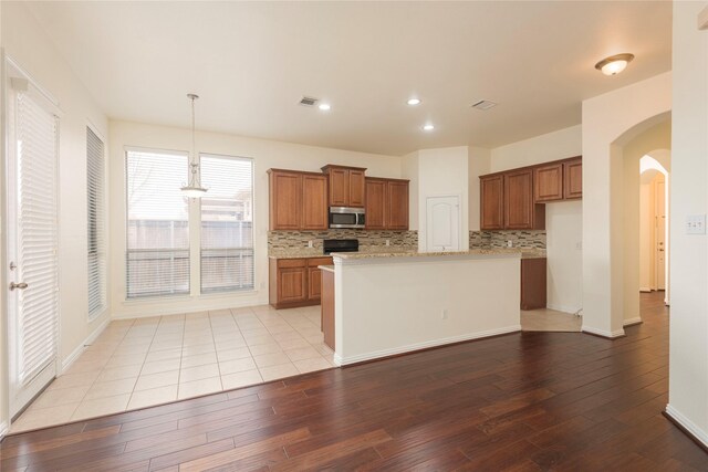 211 Wooded Creek Ave, Wylie, TX 75098 - kitchen featuring stainless steel microwave, brown cabinetry, wood-type flooring, decorative backsplash, and recessed lighting