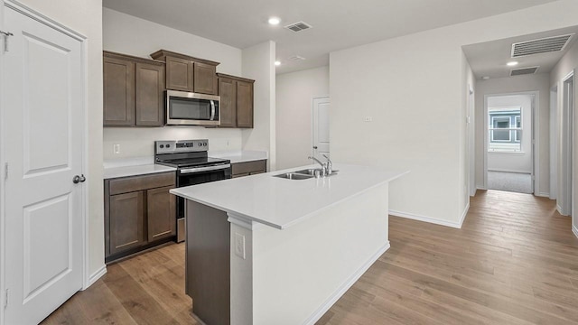 441 Drake Dr, Ferris, TX 75125 - kitchen featuring appliances with stainless steel finishes, light wood-type flooring, an island with sink, light countertops, and dark brown cabinets