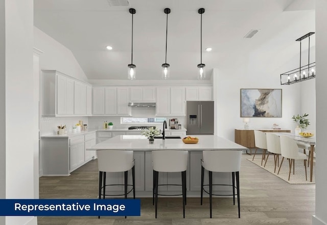 1403 Heron St, Mansfield, TX 76063 - kitchen with stainless steel appliances, light wood-style flooring, under cabinet range hood, white cabinets, and an island with sink