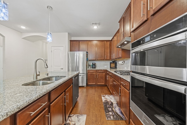 2025 Meliana Dr, Little Elm, TX 75068 - kitchen featuring stainless steel appliances, under cabinet range hood, wood finished floors, light stone counters, and hanging light fixtures