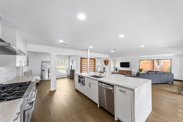 12211 Quincy Ln, Dallas, TX 75230 - kitchen featuring appliances with stainless steel finishes, white cabinetry, light wood-style floors, an island with sink, and recessed lighting