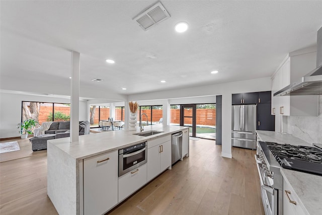 12211 Quincy Ln, Dallas, TX 75230 - kitchen with appliances with stainless steel finishes, wall chimney exhaust hood, plenty of natural light, light wood finished floors, and recessed lighting