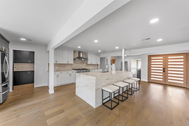 12211 Quincy Ln, Dallas, TX 75230 - kitchen featuring wall chimney range hood, light wood finished floors, decorative backsplash, stainless steel refrigerator, and recessed lighting
