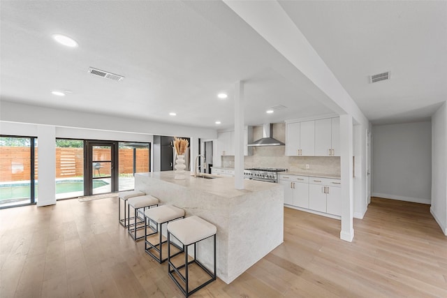 12211 Quincy Ln, Dallas, TX 75230 - kitchen featuring wall chimney range hood, high end range, light wood-style floors, white cabinets, and recessed lighting