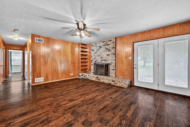 12906 Fm 902, Dorchester, TX 75459 - unfurnished living room featuring hardwood / wood-style flooring, ceiling fan, wood walls, a brick fireplace, and a textured ceiling