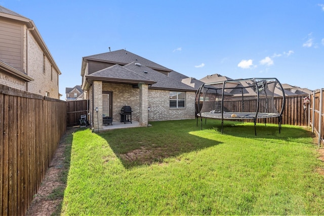 18137 Lakefront Ct, Forney, TX 75126 - back of property with a shingled roof, brick siding, a trampoline, a fenced backyard, and a patio