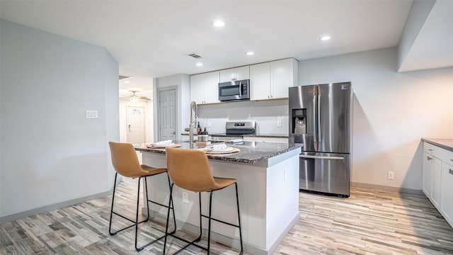 1031 Oak Hurst Dr, Grapevine, TX 76051 - kitchen featuring appliances with stainless steel finishes, light wood-style floors, a kitchen island with sink, white cabinetry, and a breakfast bar area