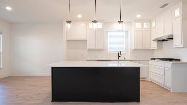 1032 Meadowlark, Forney, TX 75126 - kitchen featuring under cabinet range hood, stainless steel gas stovetop, a kitchen island, tasteful backsplash, and light wood-style flooring