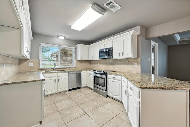 1208 Homestead St, Flower Mound, TX 75028 - kitchen featuring appliances with stainless steel finishes, a peninsula, white cabinetry, tasteful backsplash, and light tile patterned flooring