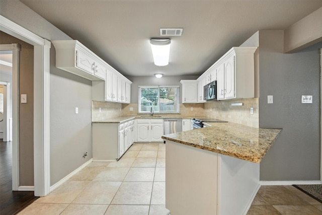 1208 Homestead St, Flower Mound, TX 75028 - kitchen with a peninsula, appliances with stainless steel finishes, decorative backsplash, light stone counters, and white cabinets