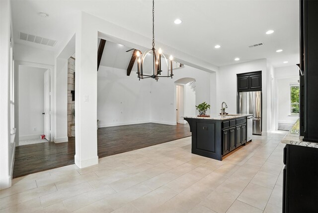 1312 Bluebell Ave, Lantana, TX 76226 - kitchen featuring freestanding refrigerator, arched walkways, a chandelier, a center island with sink, and light stone counters
