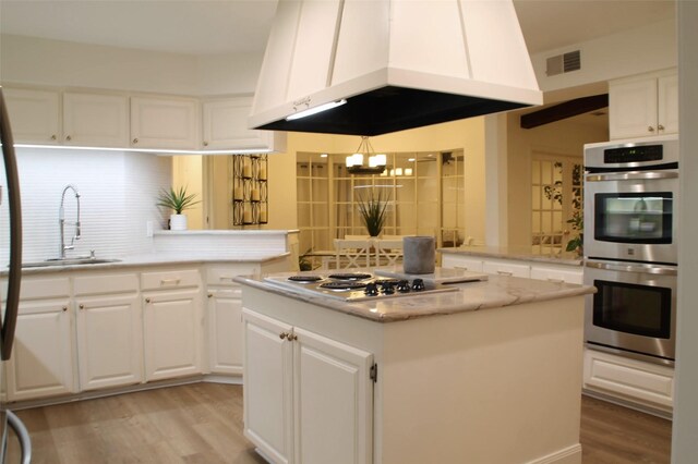 3205 Cortez Ct W, Irving, TX 75062 - kitchen with stainless steel appliances, ventilation hood, light wood-style flooring, a kitchen island, and decorative backsplash