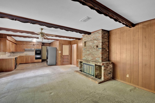 3053 Pines Rd, Shreveport, LA 71119 - unfurnished living room with wood walls, beamed ceiling, light carpet, a brick fireplace, and a ceiling fan
