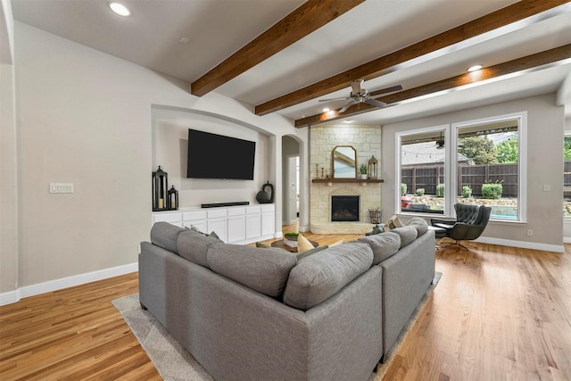 5705 Heron Dr E, Colleyville, TX 76034 - living area featuring light wood-type flooring, a stone fireplace, arched walkways, a ceiling fan, and beam ceiling