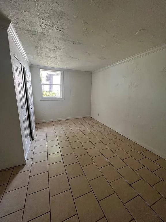 705 W Green St, Palestine, TX 75801 - unfurnished bedroom with crown molding, light tile patterned floors, and a textured ceiling