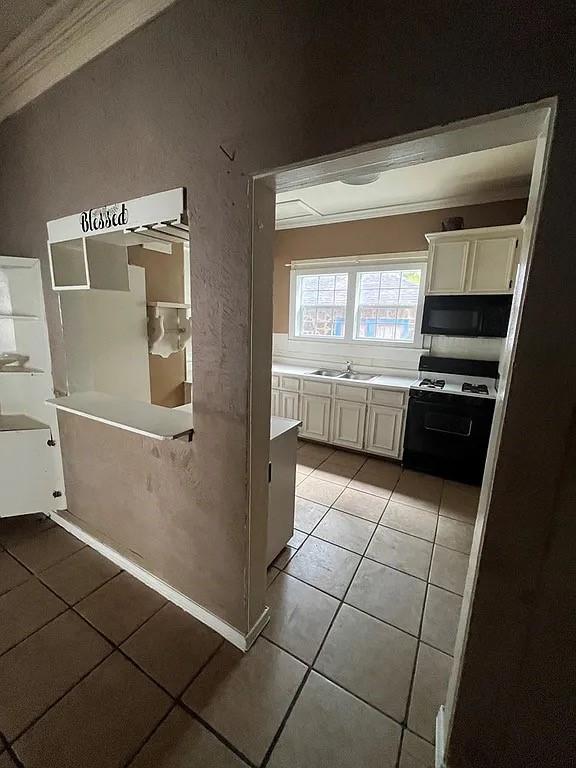 705 W Green St, Palestine, TX 75801 - kitchen with gas range, light tile patterned floors, light countertops, white cabinets, and crown molding