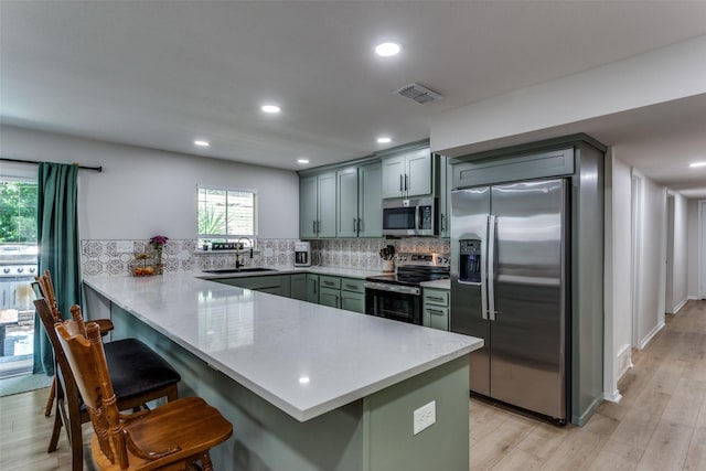 4105 Micki Lynn Ave, Fort Worth, TX 76107 - kitchen featuring appliances with stainless steel finishes, a peninsula, a kitchen bar, decorative backsplash, and light wood-style flooring