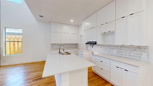 3418 Borger St, Dallas, TX 75212 - kitchen with backsplash, a center island with sink, light wood-type flooring, recessed lighting, and white cabinets