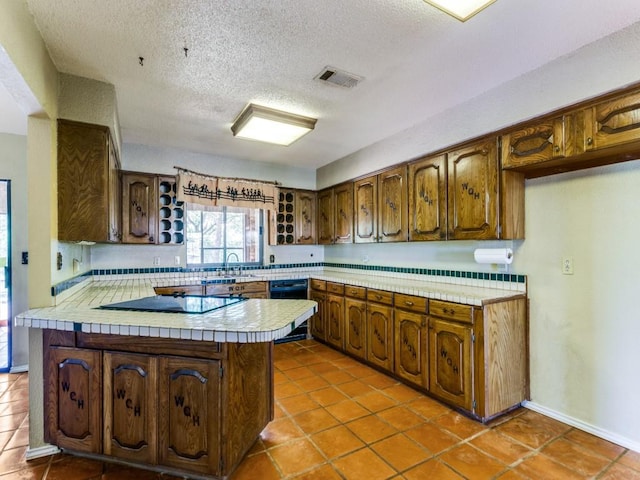 5403 Oakridge Rd, Joshua, TX 76058 - kitchen with black appliances, a peninsula, tile patterned flooring, a textured ceiling, and brown cabinetry