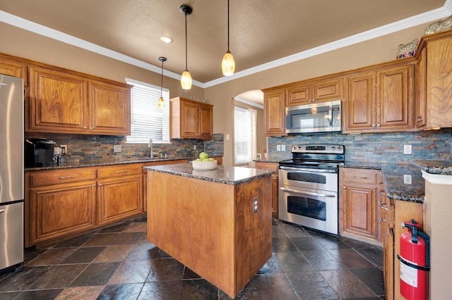 701 Champlain Ct, Midlothian, TX 76065 - kitchen featuring appliances with stainless steel finishes, a kitchen island, brown cabinetry, backsplash, and arched walkways