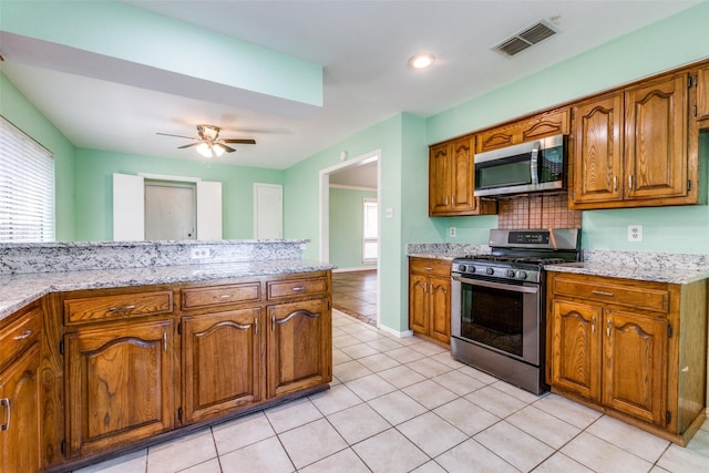 1308 Choctaw Dr, Mesquite, TX 75149 - kitchen featuring appliances with stainless steel finishes, brown cabinets, light tile patterned floors, ceiling fan, and decorative backsplash