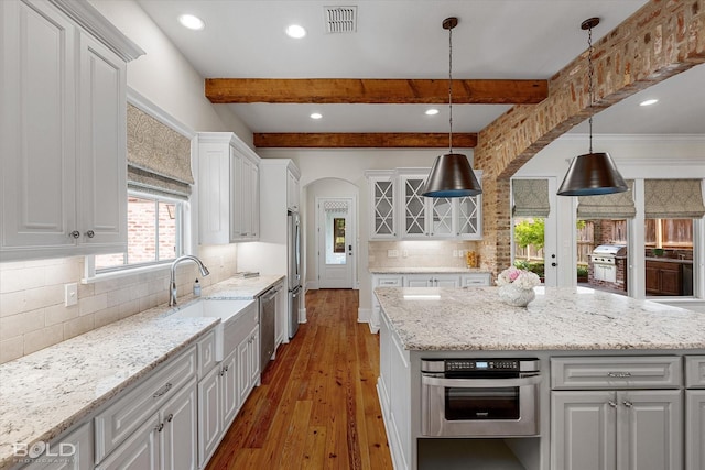 1030 Winterberry Ln, Shreveport, LA 71106 - kitchen featuring arched walkways, wood-type flooring, stainless steel appliances, white cabinetry, and beamed ceiling